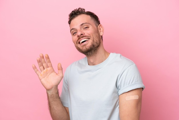 Jonge braziliaanse man met pleisters geïsoleerd op roze achtergrond saluerend met de hand met gelukkige uitdrukking