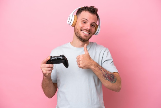 Jonge braziliaanse man spelen met video game controller geïsoleerd op roze achtergrond met een duim omhoog gebaar