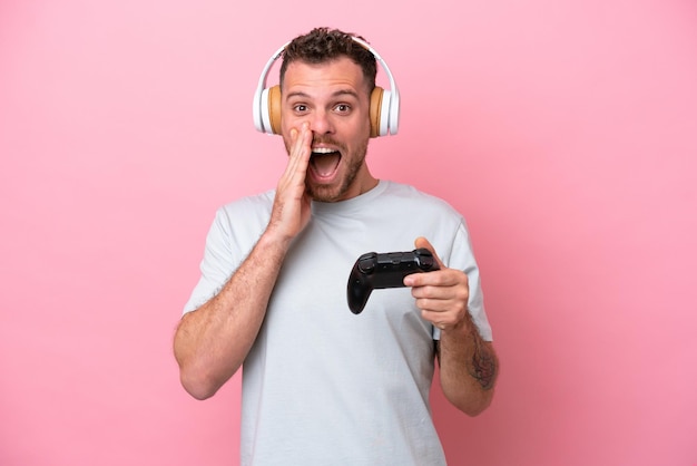 Jonge Braziliaanse man spelen met video game controller geïsoleerd op roze achtergrond met verrassing en geschokte gezichtsuitdrukking