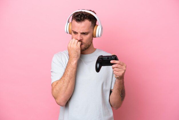 Jonge Braziliaanse man spelen met video game controller geïsoleerd op roze achtergrond twijfels