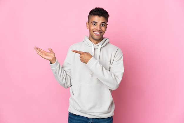 Jonge Braziliaanse mens die op roze ruimte wordt geïsoleerd die copyspace denkbeeldig op de palm houdt om een advertentie in te voegen