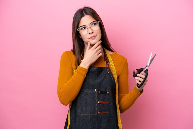 Jonge Braziliaanse naaistervrouw die op roze achtergrond wordt geïsoleerd die twijfels heeft