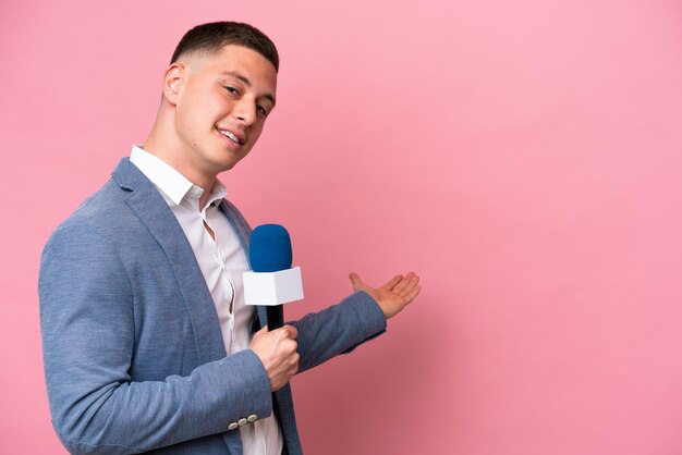 Jonge Braziliaanse presentator geïsoleerd op een roze achtergrond die zijn handen naar de zijkant uitstrekt om uit te nodigen om te komen