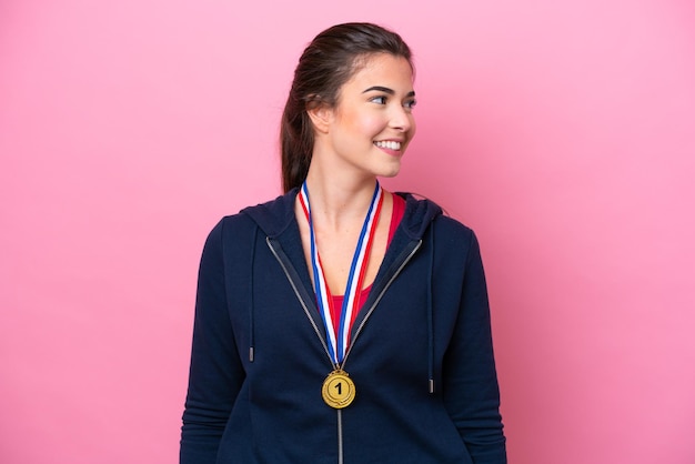 Jonge Braziliaanse sportvrouw met medailles die op roze achtergrond wordt geïsoleerd die kant kijkt