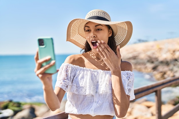 Jonge braziliaanse vrouw die een selfie-foto maakt met smartphone buiten bang en verbaasd met open mond van verbazing, ongeloof gezicht