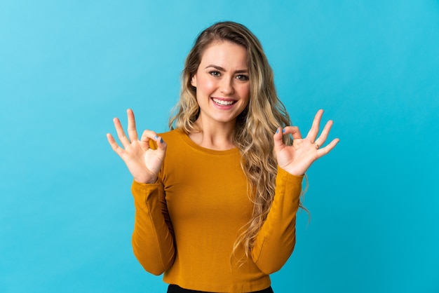 Jonge Braziliaanse vrouw die op blauw wordt geïsoleerd dat ok teken met twee handen toont