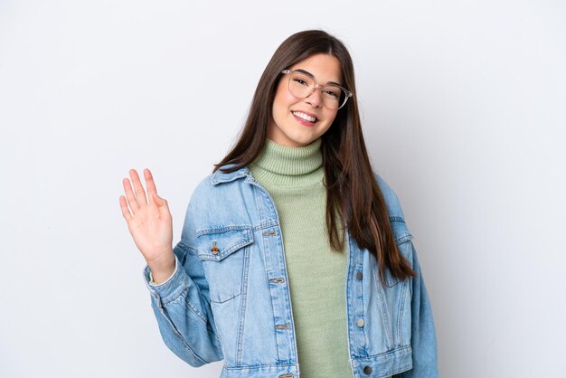 Jonge Braziliaanse vrouw die op witte achtergrond wordt geïsoleerd die met hand met gelukkige uitdrukking salueert