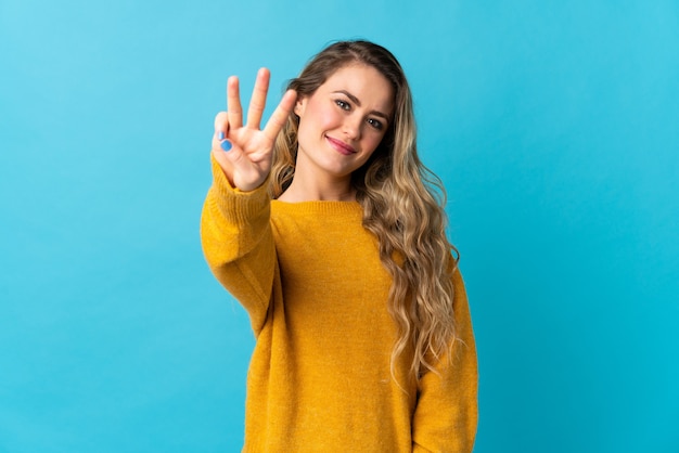 Jonge Braziliaanse vrouw geïsoleerd op blauw gelukkig en drie tellen met vingers