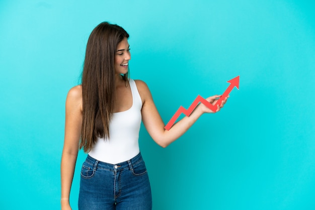 Jonge Braziliaanse vrouw geïsoleerd op een blauwe achtergrond die een stijgende pijl vasthoudt met een gelukkige uitdrukking