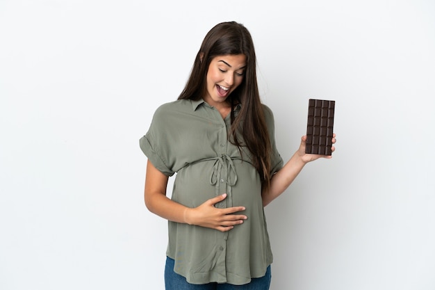 Jonge Braziliaanse vrouw geïsoleerd op een witte achtergrond zwanger en houden van chocolade met verbaasde expression