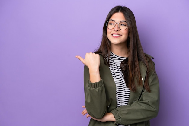 Jonge Braziliaanse vrouw geïsoleerd op paarse achtergrond wijst naar de zijkant om een product te presenteren