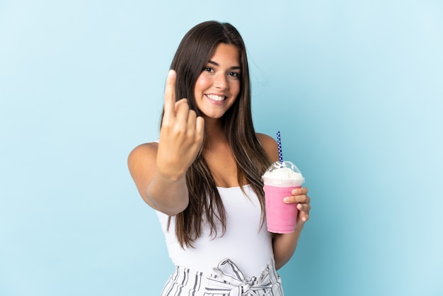 Jonge Braziliaanse vrouw met aardbeimilkshake die op blauwe muur wordt geïsoleerd die komend gebaar doet