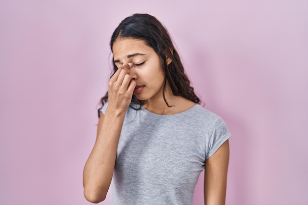 Jonge braziliaanse vrouw met casual t-shirt over roze achtergrond moe wrijvende neus en ogen die vermoeidheid en hoofdpijn voelen. stress en frustratie concept.