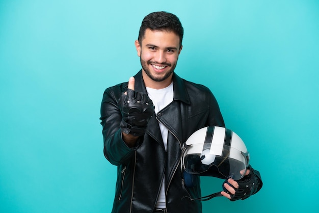 Jonge Braziliaanse vrouw met een motorhelm die op blauwe achtergrond wordt geïsoleerd die komend gebaar doet