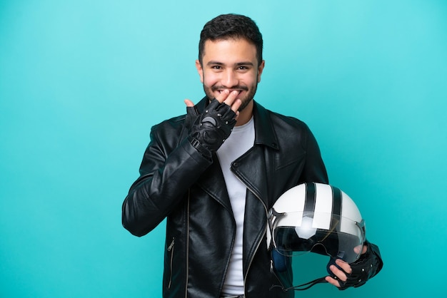 Jonge Braziliaanse vrouw met een motorhelm geïsoleerd op een blauwe achtergrond, gelukkig en glimlachend die de mond bedekt met de hand