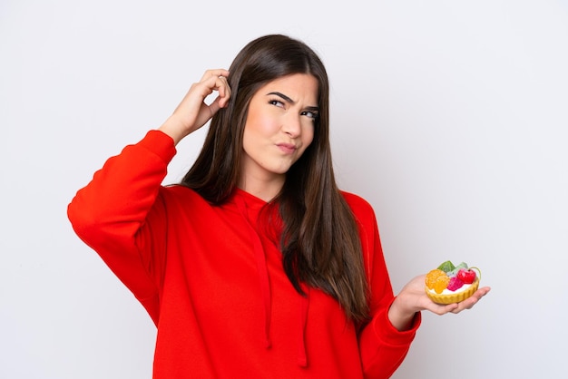 Jonge Braziliaanse vrouw met een taartje geïsoleerd op een witte achtergrond met twijfels en met verwarde gezichtsuitdrukking