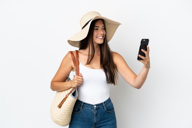 Jonge Braziliaanse vrouw met Pamela die een strandtas houdt die op witte achtergrond wordt geïsoleerd en een selfie maakt