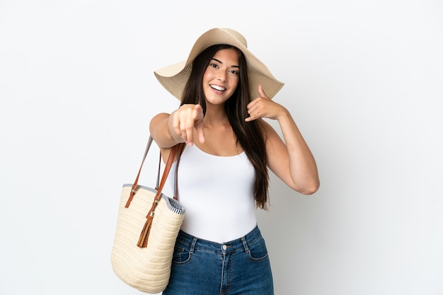 Jonge Braziliaanse vrouw met Pamela die een strandtas vasthoudt die op een witte achtergrond wordt geïsoleerd en een telefoongebaar maakt en naar voren wijst