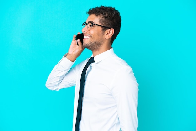 Jonge Braziliaanse zakenman geïsoleerd op blauwe achtergrond die een gesprek voert met de mobiele telefoon