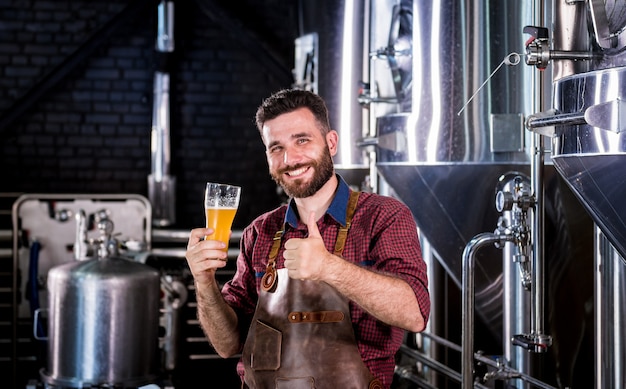 Jonge brouwer die een leren schort draagt, test bier in een moderne brouwerij