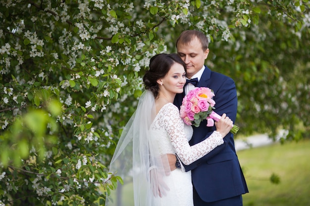 Jonge bruidegom en bruid met huwelijksboeket in bloeiende tuin