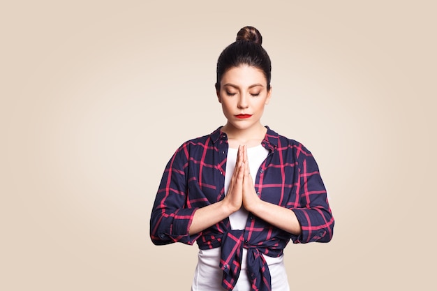 Jonge brunete vrouw die yoga beoefent, handen vasthoudt in namaste en haar ogen gesloten houdt. kaukasisch meisje dat binnenshuis mediteert, bidt voor vrede en liefde, kalme en vredige gezichtsuitdrukking heeft.