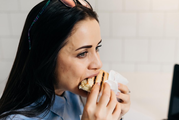 Jonge brunette freelancer meisje in blauw shirt lunchen in café na het werk