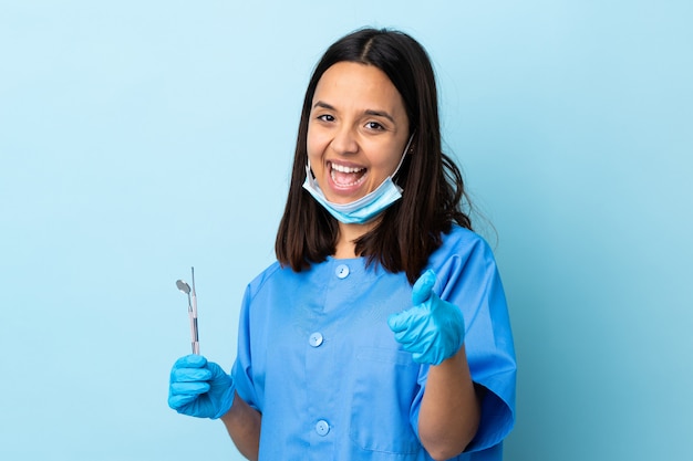 Foto jonge brunette gemengd ras tandarts vrouw met tools over geïsoleerd met duimen omhoog omdat er iets goeds is gebeurd