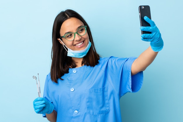 Jonge brunette gemengd ras tandarts vrouw met tools over geïsoleerde muur maken van een selfie