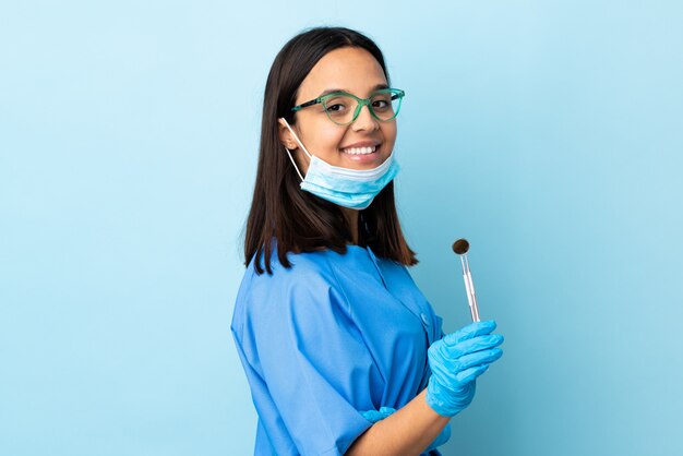 Jonge brunette gemengd ras tandarts vrouw met tools over muur met armen gekruist en vooruit kijken