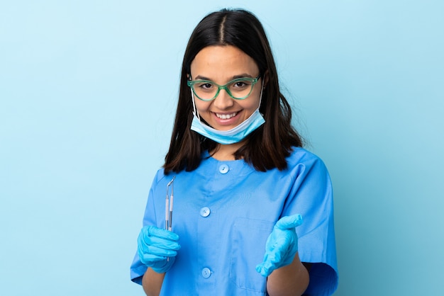 Jonge brunette gemengd ras tandarts vrouw met tools over muur schudden handen voor het sluiten van een goede deal