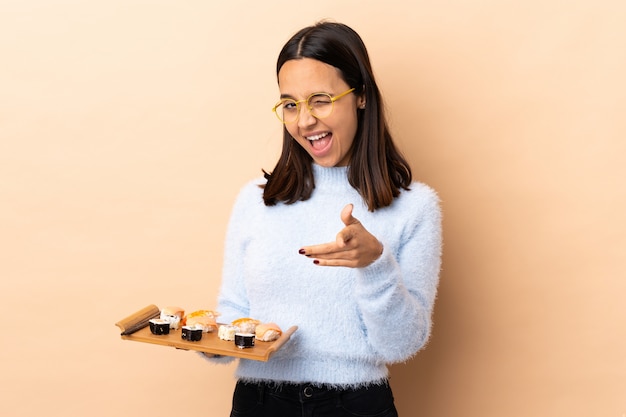 Foto jonge brunette gemengd ras vrouw met sushi over geïsoleerde wijzen naar de voorkant en glimlachen