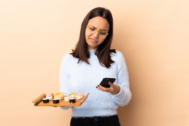 Jonge brunette gemengd ras vrouw met sushi over muur denken en het verzenden van een bericht