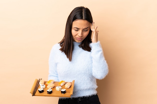 Jonge brunette gemengde ras vrouw met sushi over geïsoleerde muur met hoofdpijn