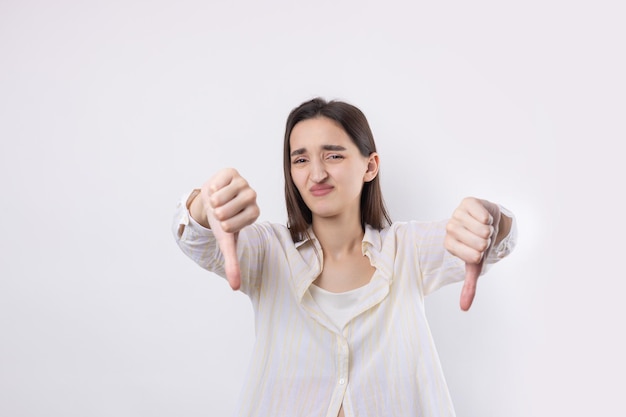 Jonge brunette in een blauwe tanktop die een duim omlaag gebaar geeft met een negatieve uitdrukking