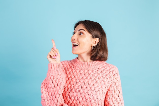 Jonge brunette in warme roze trui geïsoleerd op blauwe muur