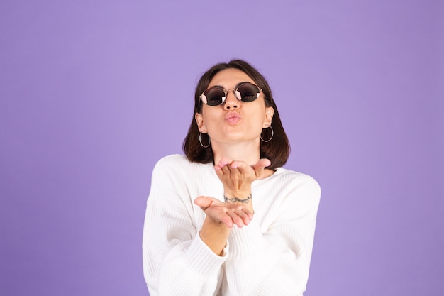 Jonge brunette in witte casual trui geïsoleerd op paarse muur