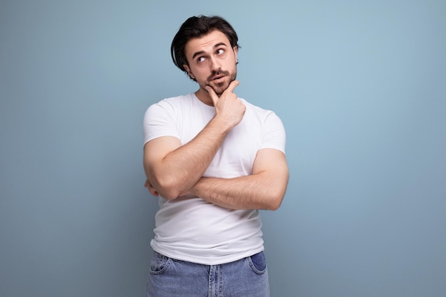 Jonge brunette man in een wit t-shirt dacht terwijl hij op een studioachtergrond stond