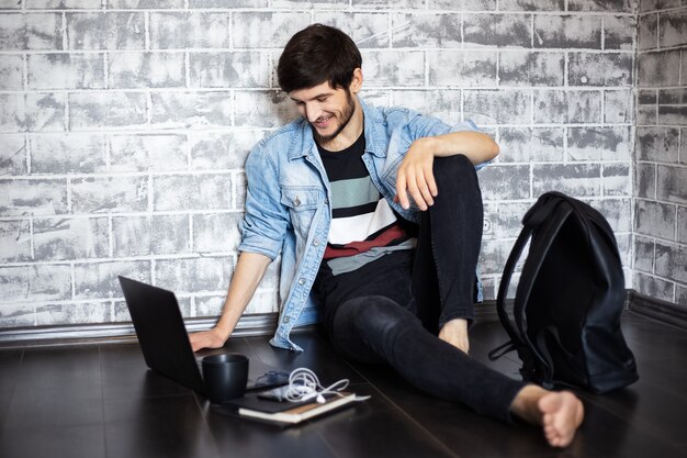 Jonge brunette man zittend op de vloer met laptop en smartphone op de