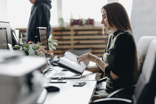 Jonge brunette meid gekleed in kleding in kantoorstijl zit aan het bureau en houdt het notitieboekje in haar handen als een licht modern kantoor