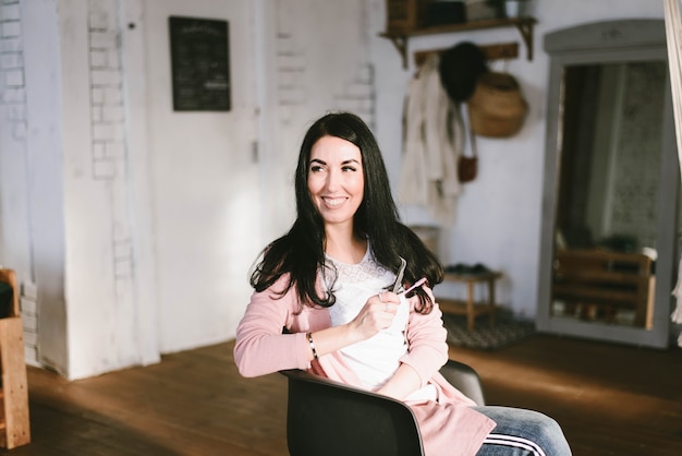 Jonge brunette meisje in een roze trui en wit t-shirt lacht zittend in een stoel