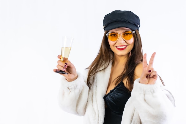 Jonge brunette meisje in zwarte hoed vieren oudejaarsavond op een witte achtergrond. Ik daag het model uit met een heel vrolijk glas champagne