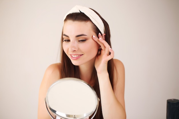 Jonge brunette vrouw doet haar huidverzorging in de spiegel