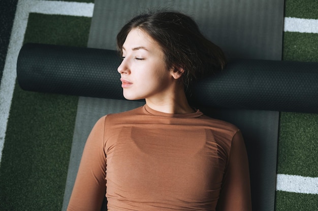 Jonge brunette vrouw doet stretching pilates op massage roll in de sportschool van de fitnessclub