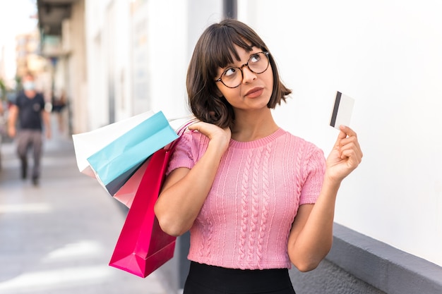 Jonge brunette vrouw in de stad met boodschappentassen en een creditcard en denken