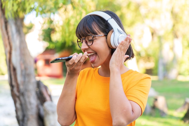 Jonge brunette vrouw in het park muziek luisteren met een mobiel en zingen
