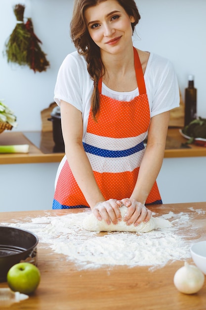 Jonge brunette vrouw koken pizza of handgemaakte pasta in de keuken. Huisvrouw bereidt deeg op houten tafel. Dieet, voedsel en gezondheidsconcept.