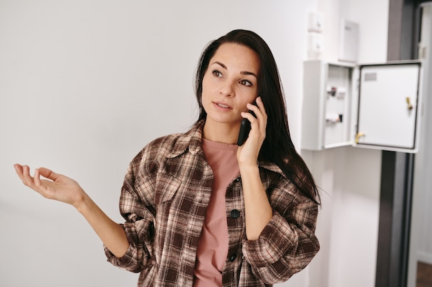 Jonge brunette vrouw legt haar probleem op mobiele telefoon uit terwijl ze een loodgieter belt