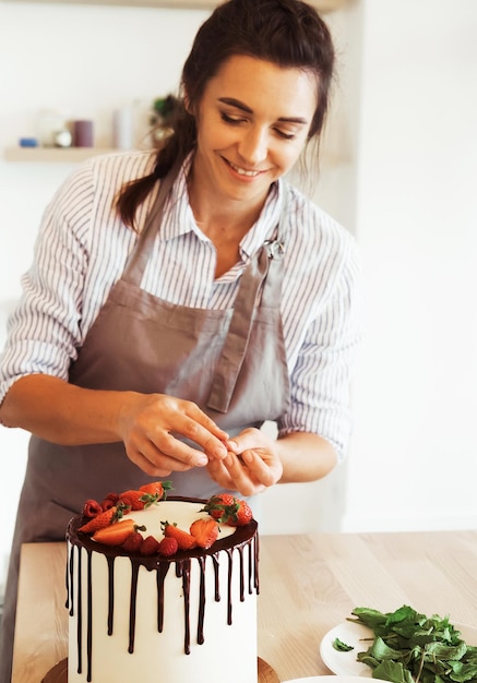 Jonge brunette vrouw maakt koekjescake met chocolade en aardbeien in de keuken