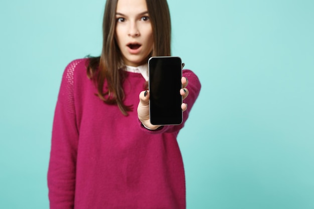 Jonge brunette vrouw meisje in casual kleding poseren geïsoleerd op blauw groene turquoise muur achtergrond studio portret. Mensen oprechte emoties levensstijl concept. Bespotten kopie ruimte. Houd mobiele telefoon vast.